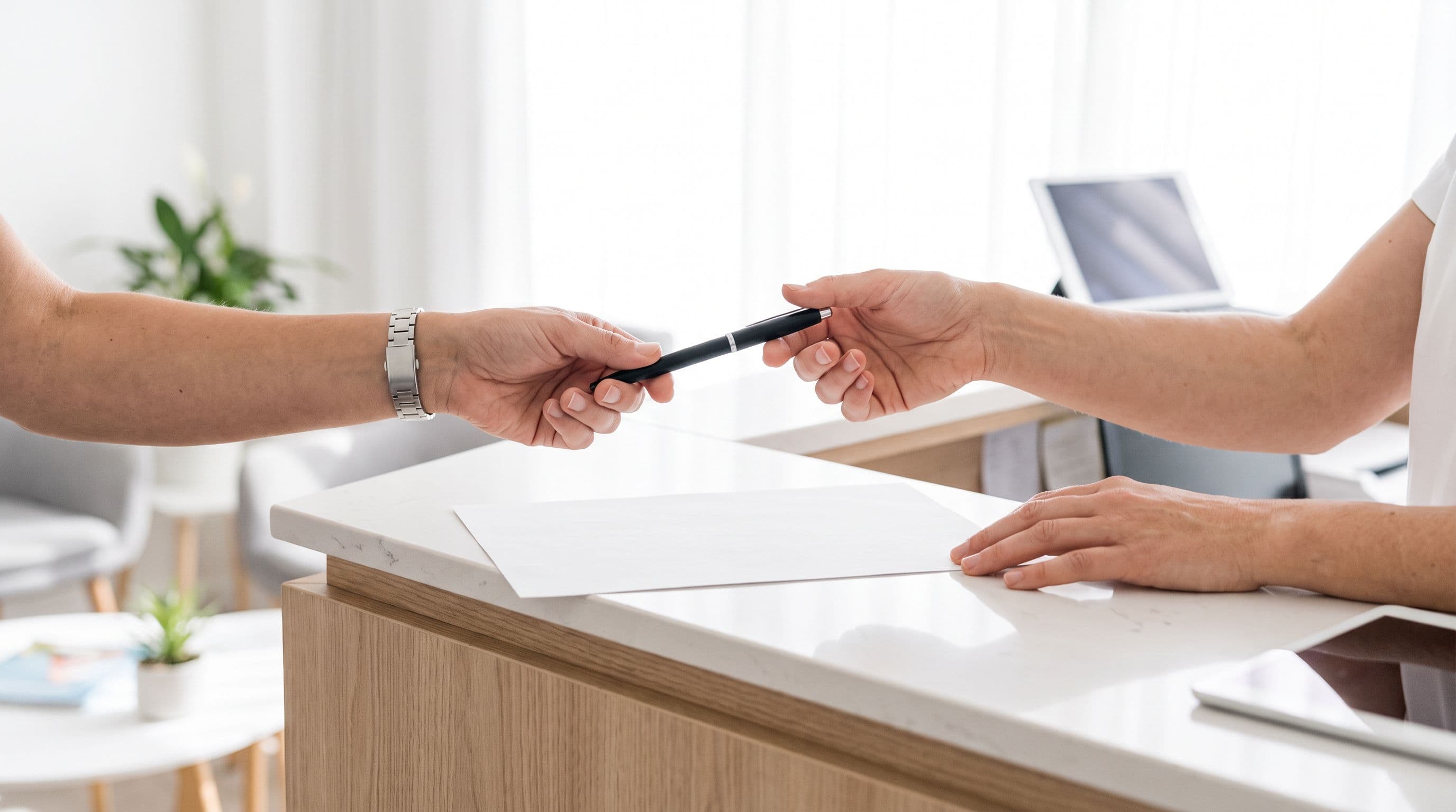 Two pairs of hands at a clinic counter across a single sheet of paper, one offering a pen